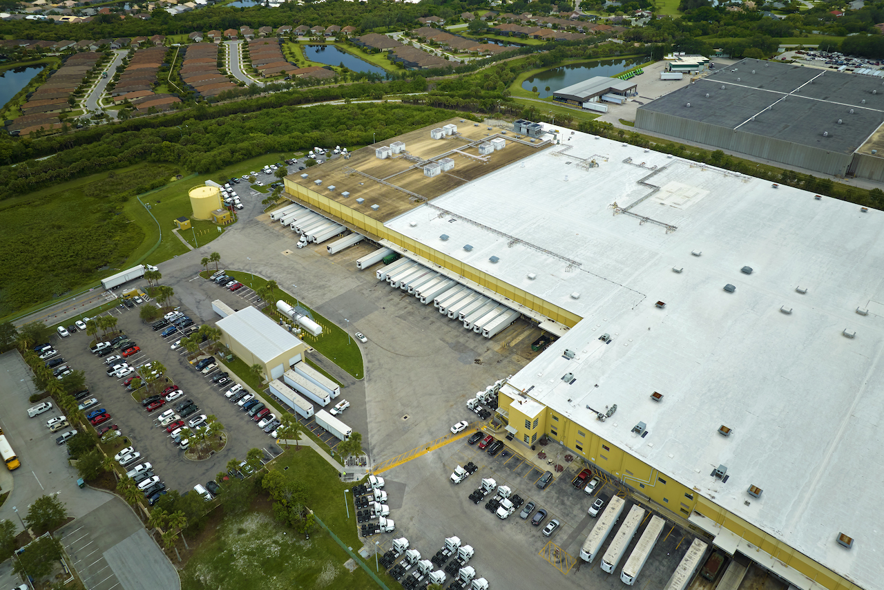 Aerial view of large commercial distribution center with many trucks unloading and uploading retail products for further shipment. Global economy concept